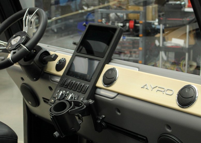 AYRO electric vehicle dashboard with steering wheel, center-mounted touchscreen, and climate control knobs, shown on the production floor.